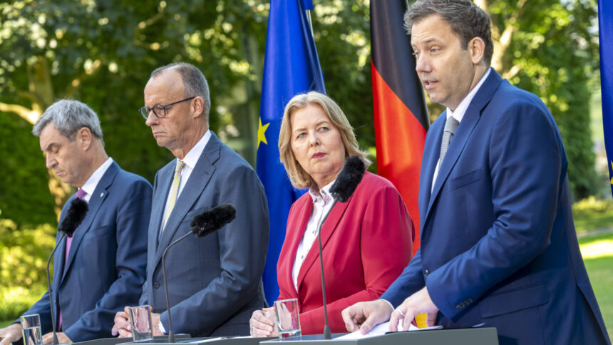 Vier Personen stehen an Rednerpulten vor den Flaggen der Europäischen Union und Deutschlands, drei Männer und eine Frau, die Frau trägt einen roten Blazer