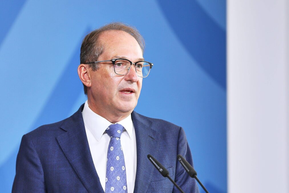 Ein Mensch mit Brille und blauer Krawatte in blauem Anzug vor einem blauen Hintergrund