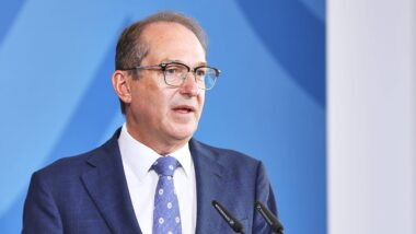 Ein Mensch mit Brille und blauer Krawatte in blauem Anzug vor einem blauen Hintergrund