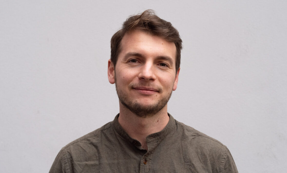 Ein Mensch in braun-beigem Hemd schaut in die Kamera.