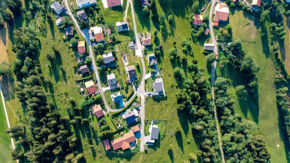 Blick von oben auf eine Siedlung mit Straßen, von Wiesen und Bäumen umringt