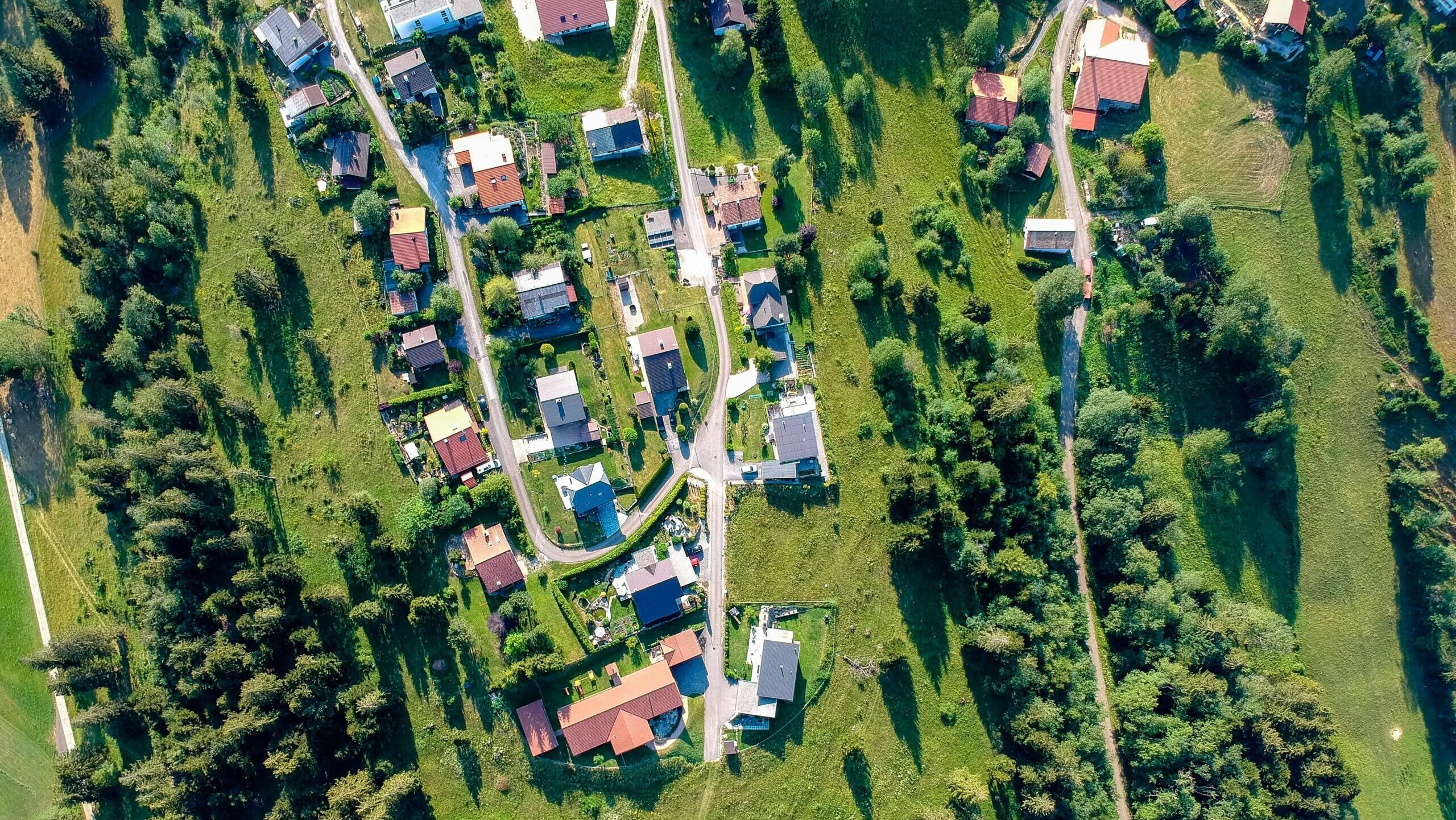 Blick von oben auf eine Siedlung mit Straßen, von Wiesen und Bäumen umringt