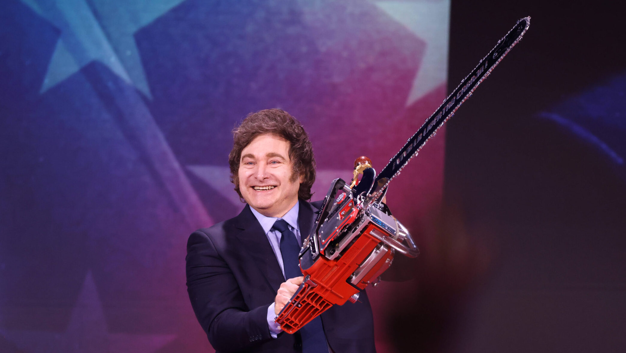 Mann in Anzug mit Locken und sonderbaren Kotletten und einer Motorsäge in der Hand