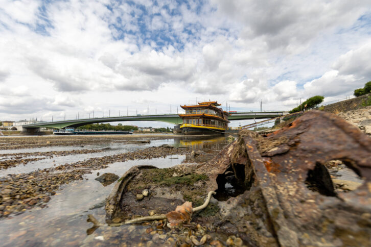 Ein fast vollständig ausgetrocknetes, breites Flussbett, ein Schiff liegt auf Grund, im Hintergrund eine Brücke