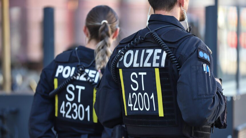 Zwei Polizist:innen, zu sehen sind ihre Rückennummern, die mit "ST" für Sachsen-Anhalt beginnen.