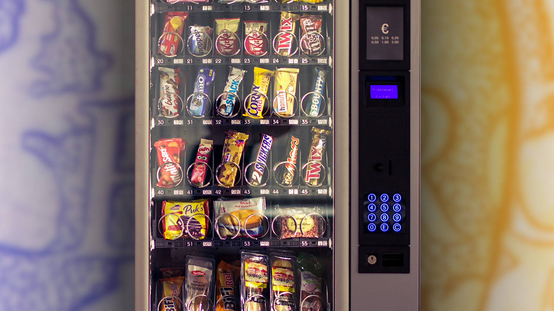 Ein Snackautomat, im Hintergrund eine blau-gelb eingefärbte Euro-Münze.
