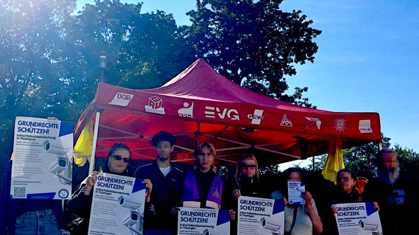 Eine Reihe von Menschen steht vor einem roten Pavillon und hält Plakate, auf denen steht: "Grundrechte schützen!"