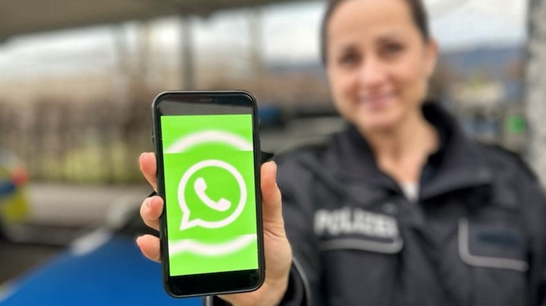 Polizistin zeigt Smartphone mit WhatsApp-Logo