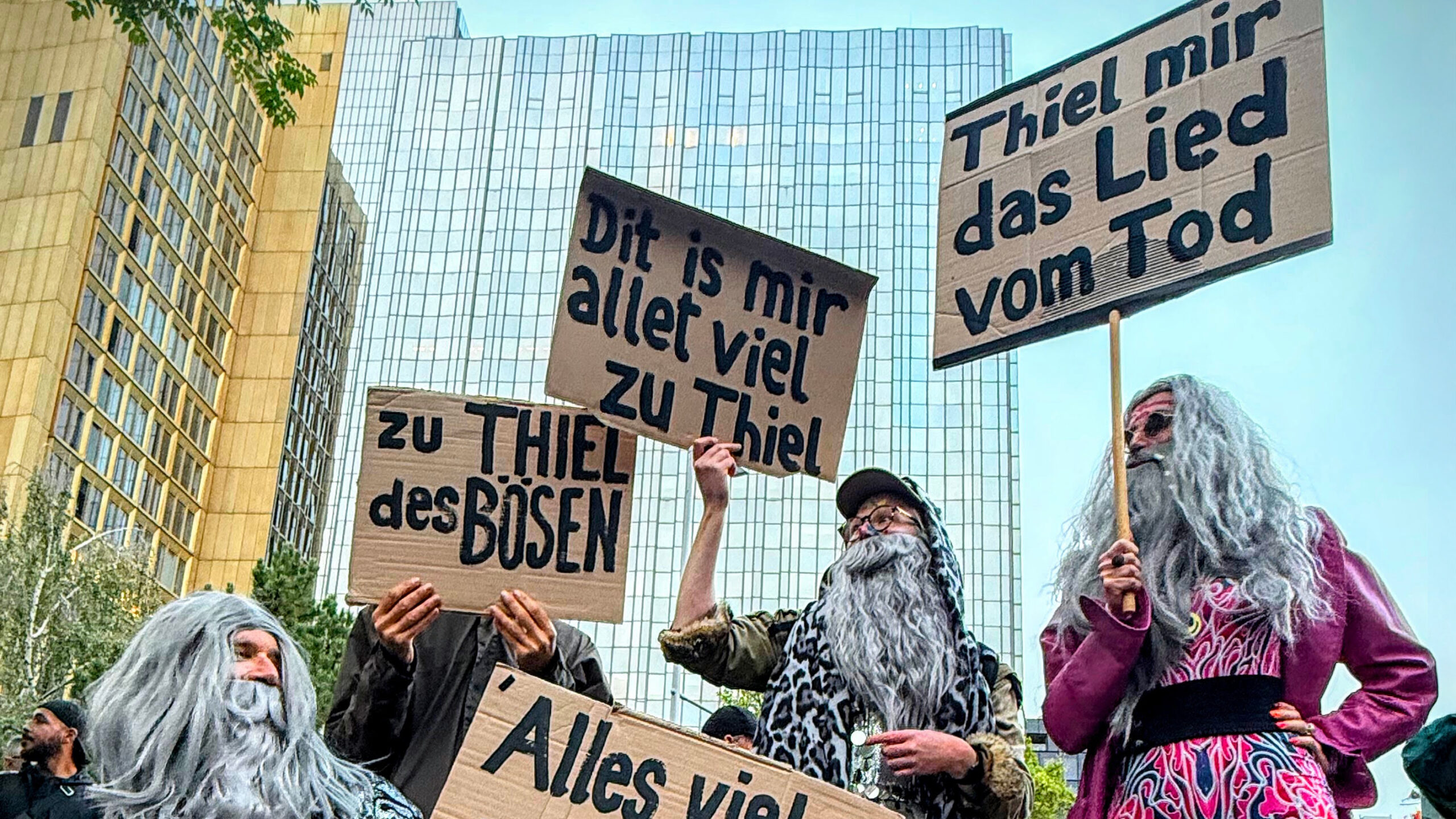 Menschen protestieren als Gandalf verkleidet vor dem Springer-Gebäude. Sie tragen Schilder mit Aufschriften wie "Thiel mir das Lied vom Tod", "Dit is mir alles zu Thiel" oder "Zu Thiel des Bösen"