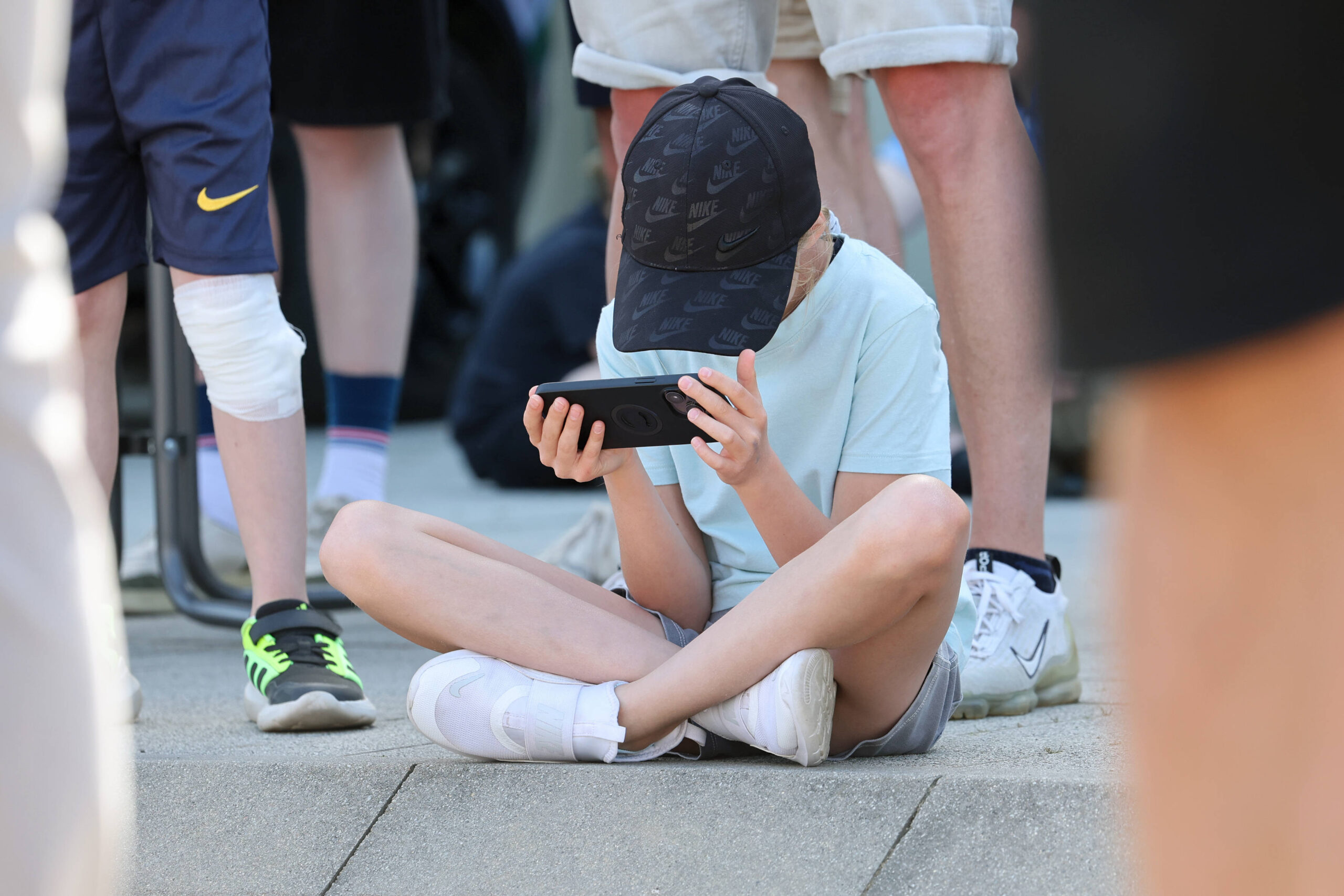 Kind sitzt auf den Boden und schaut auf Smartphone