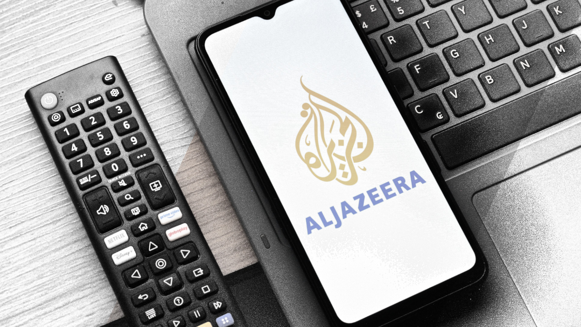 Eine Fernbedienung, einen Laptop-Tastatur, ein Smartphone mit Logo von Al Jazeera.