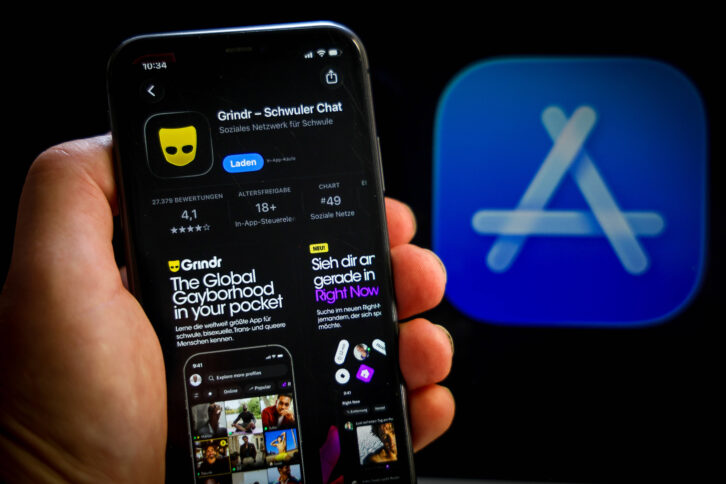 Eine Hand hält ein Smartphone in der Hand, auf dem Bildschirm ist die Präsentation der Anwendung im App-Store zu sehen, unter anderem mit dem Schriftzug "Grindr - Schwuler Chat"
