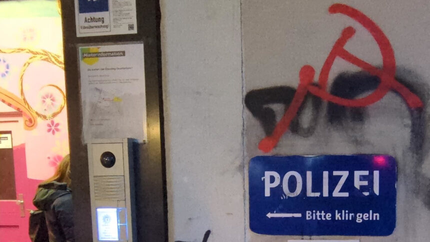 Ein blaues Schild: "Polizei - bitte klingeln". Darüber schwarzes Gesprühtes und Hammer-und-Sichel in rot.